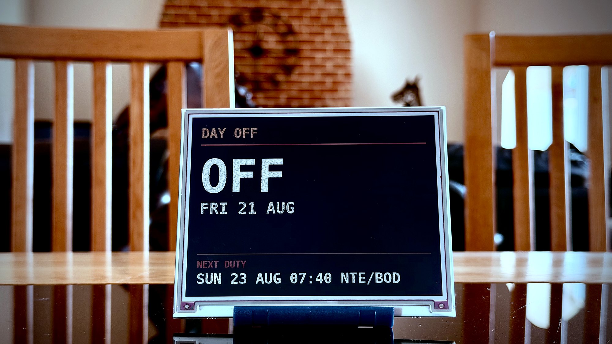 An Ident display standing on a dining table, showing DAY OFF, FRI 21 AUG, and the next duty on Sunday to NTE and BOD